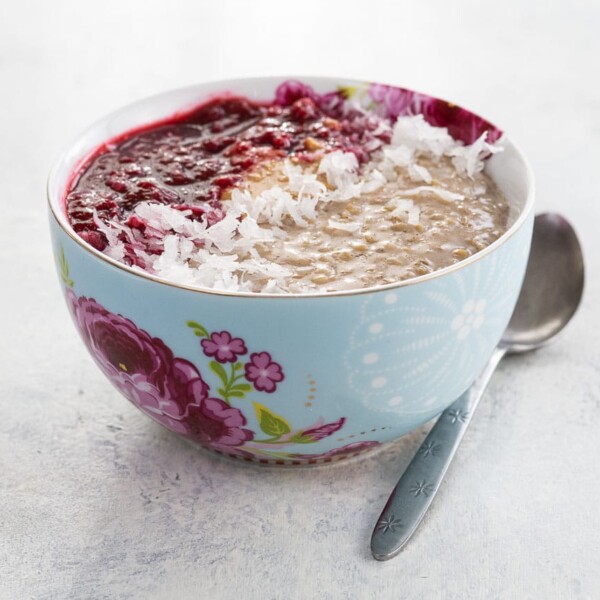 instant pot oatmeal recipe garnished with raspberry compote, peanut butter, and shredded coconut in a bowl with a spoon