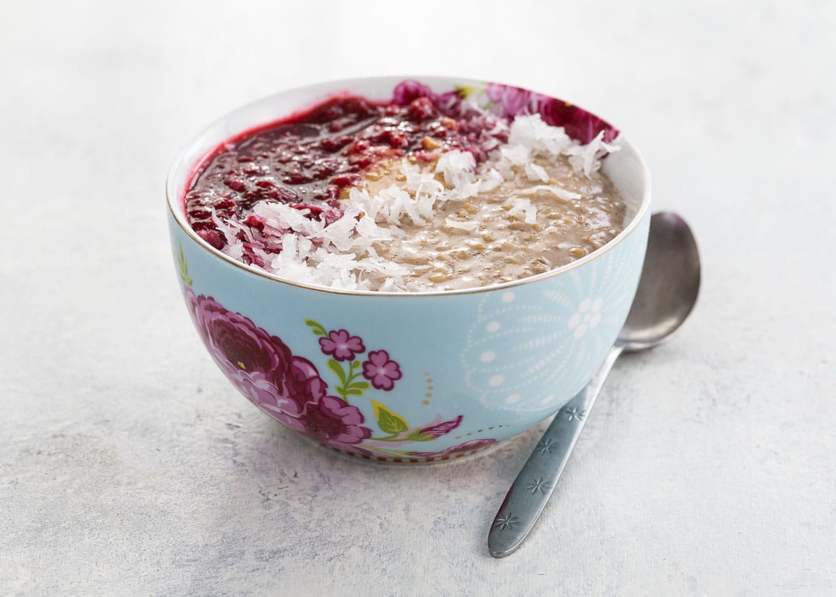 instant pot oatmeal recipe garnished with raspberry compote, peanut butter, and shredded coconut in a bowl with a spoon