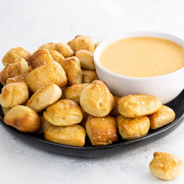 homemade soft pretzel bites on a black plate and pretzel cheese dip in a white bowl