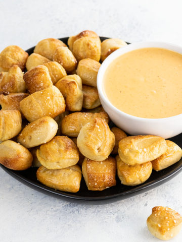 homemade soft pretzel bites on a black plate and pretzel cheese dip in a white bowl
