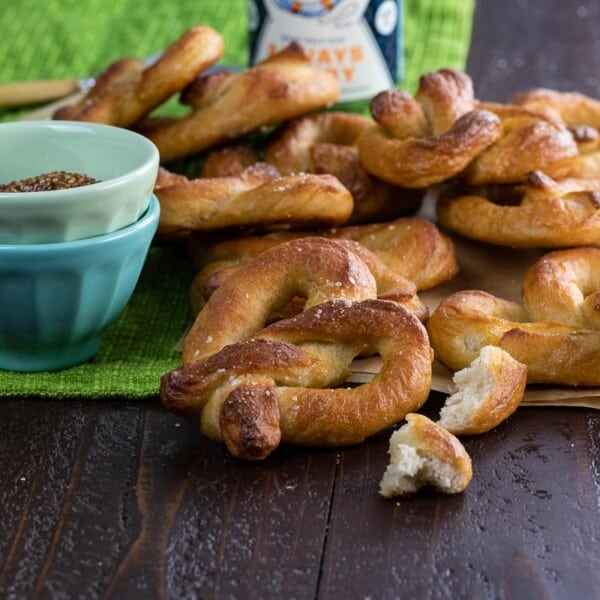 a big pile of vegan soft pretzels on a table with mustard and beer