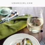 baked oysters with shallot herb butter and prosciutto on a plate with a glass of wine
