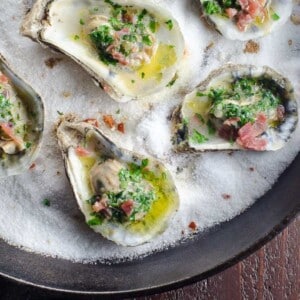 baked oysters with shallot herb butter and prosciutto on a bed of salt in a cast iron skillet