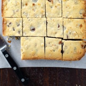 blonde brownies (white chocolate blondies with chocolate chips) on parchment with a paring knife