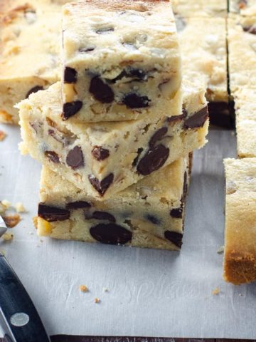 blonde brownies (white chocolate blondies with chocolate chips) on parchment with a paring knife