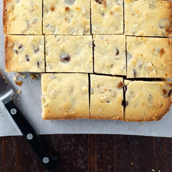 blonde brownies (white chocolate blondies with chocolate chips) on parchment with a paring knife