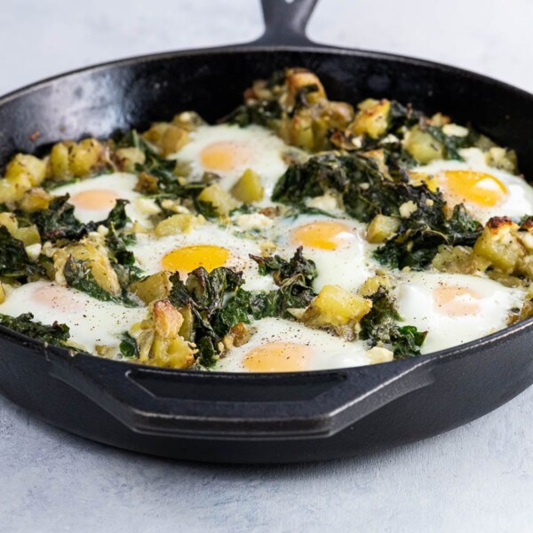baked eggs, kale, and potatoes in a cast iron skillet