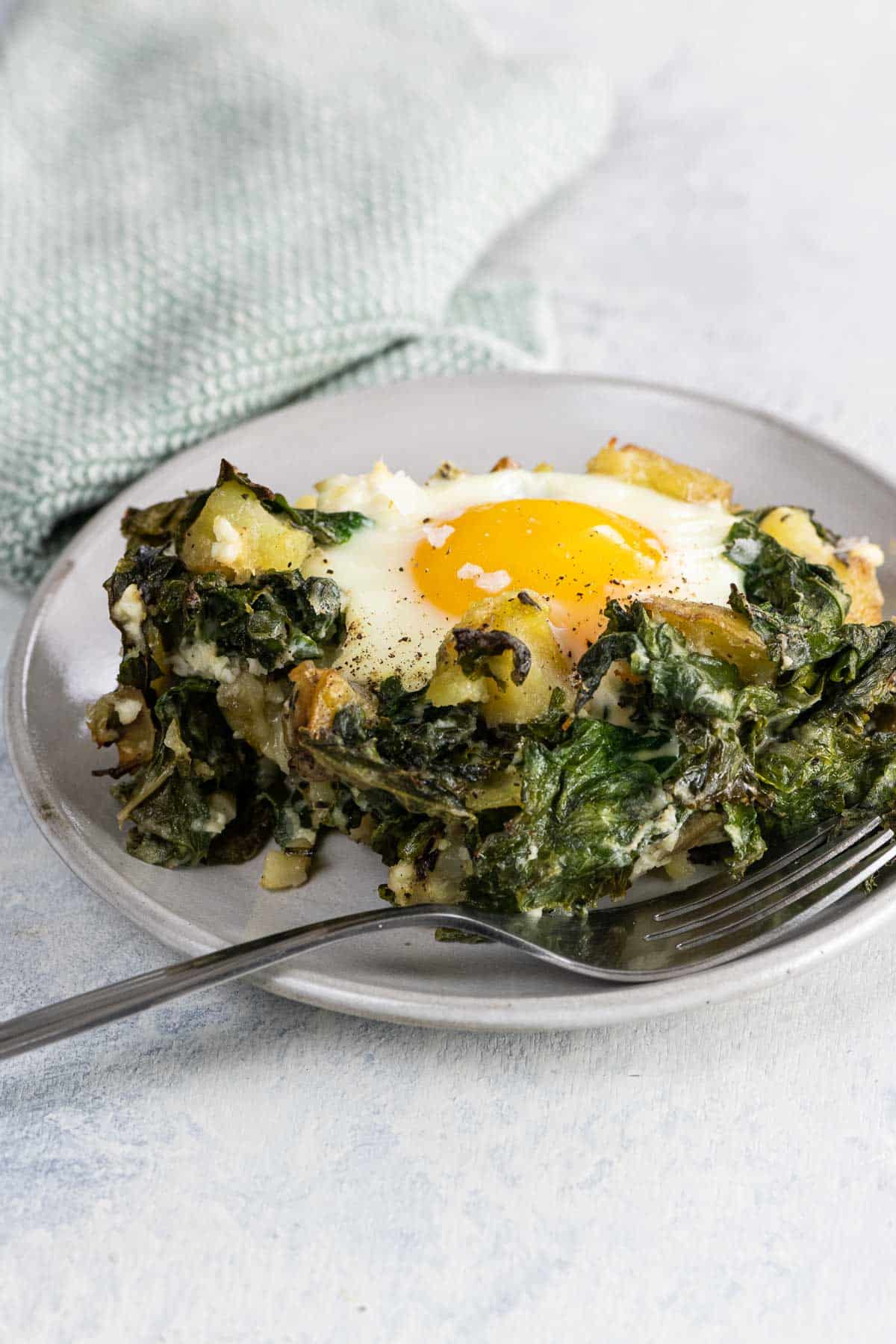 a baked egg with kale and potatoes on a plate with a fork and napkin
