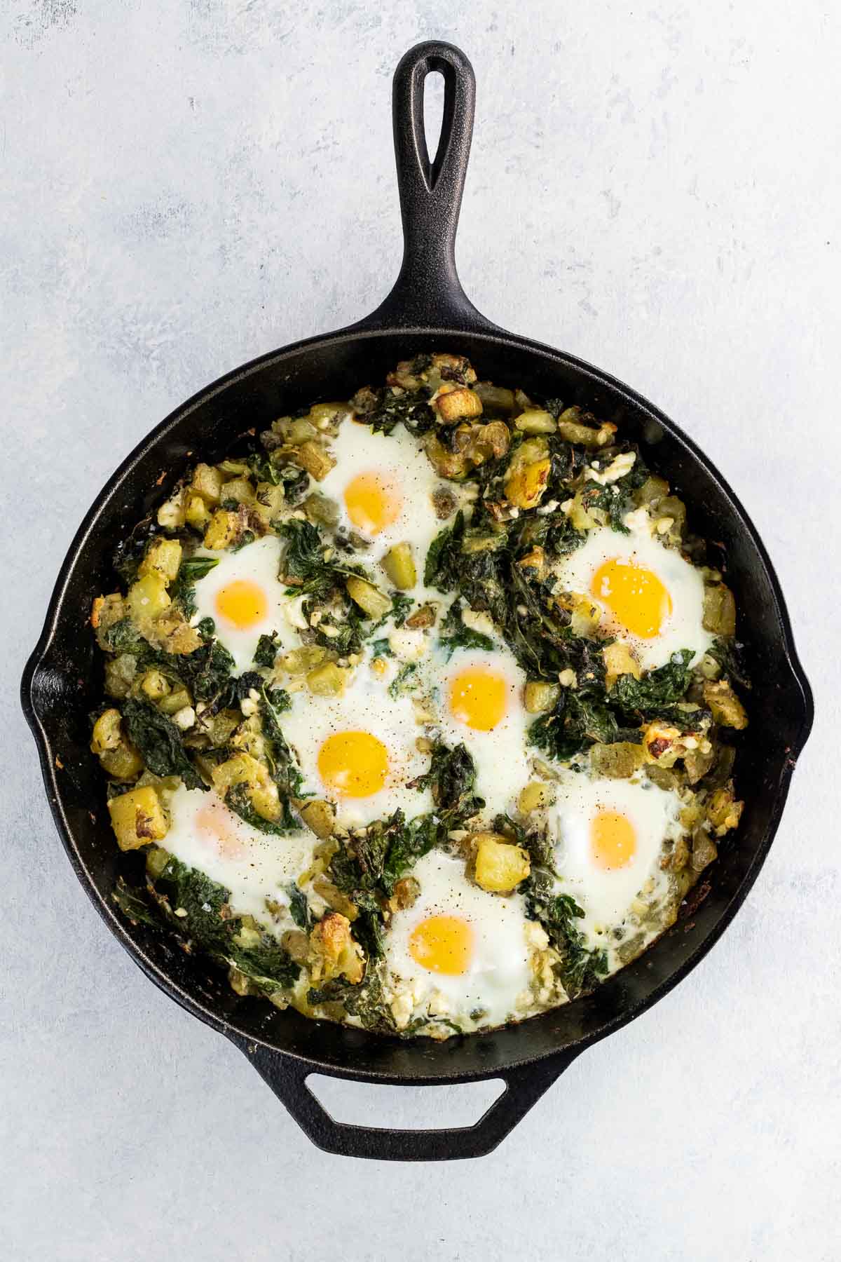 baked eggs, kale, and potatoes in a cast iron skillet