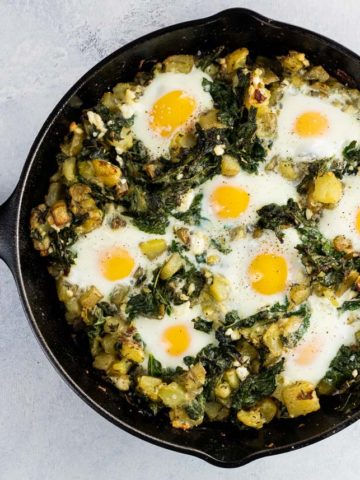 baked eggs, kale, and potatoes in a cast iron skillet