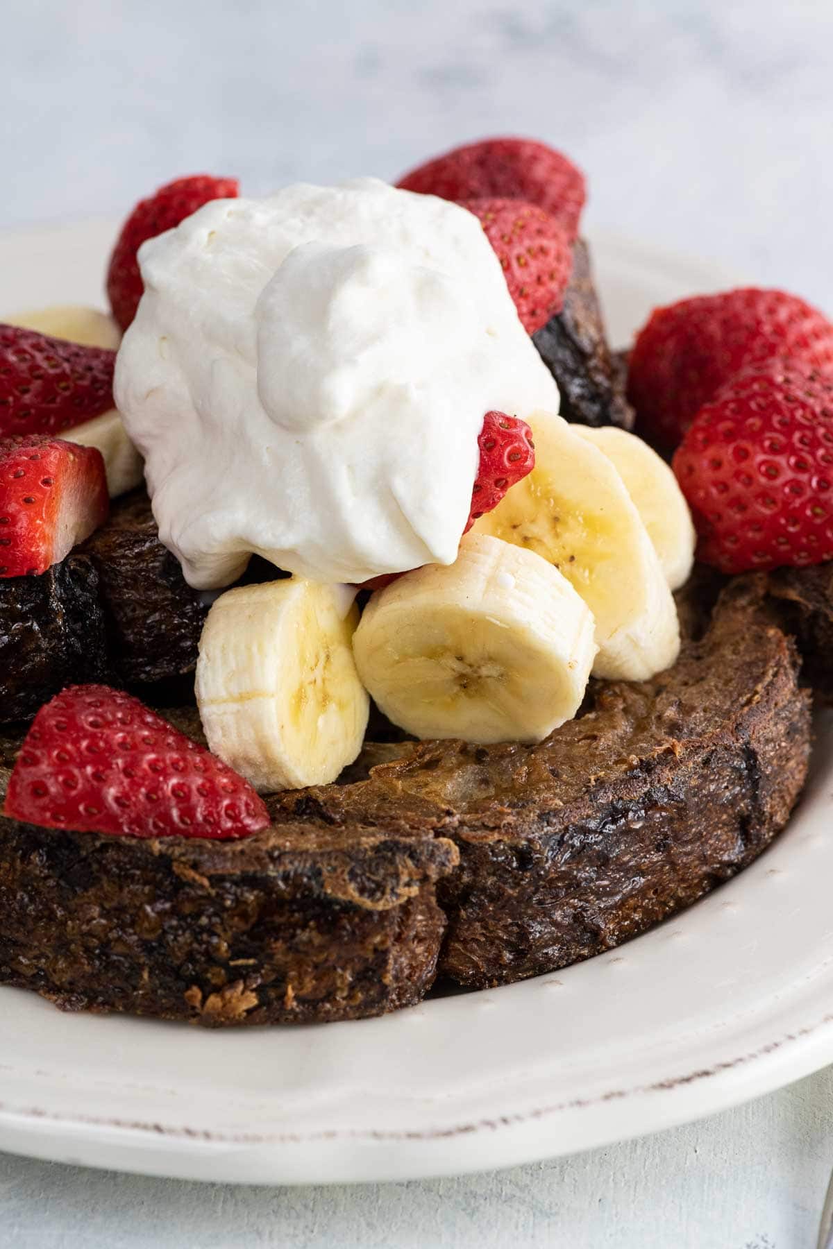 chocolate sourdough french toast with fresh fruit and whipped cream on a plate