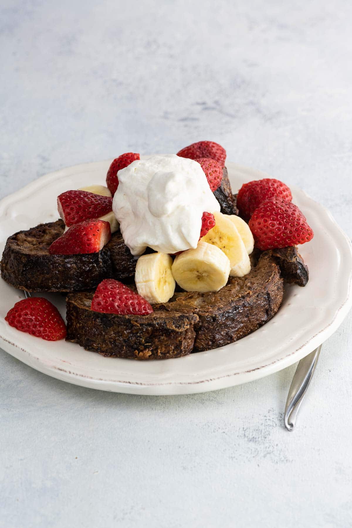 chocolate sourdough french toast with fresh fruit and whipped cream on a plate