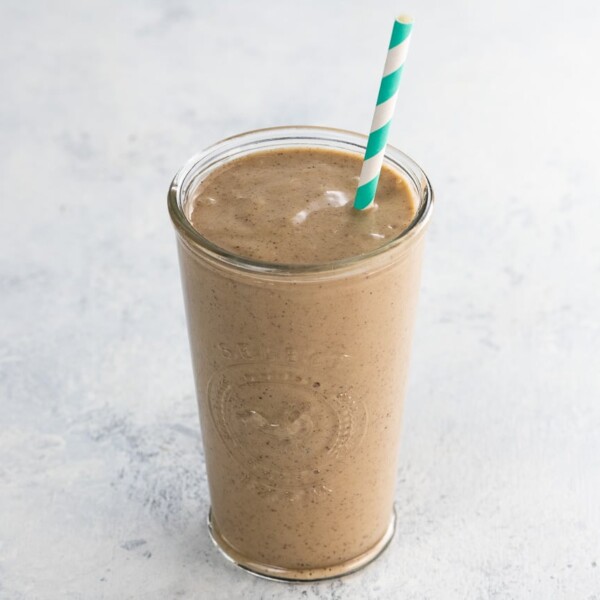 Coffee peanut butter banana smoothie in a glass with a blue and white striped straw
