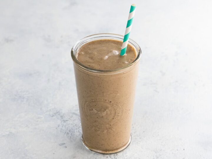 Coffee peanut butter banana smoothie in a glass with a blue and white striped straw