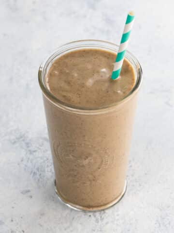 Coffee peanut butter banana smoothie in a glass with a blue and white striped straw