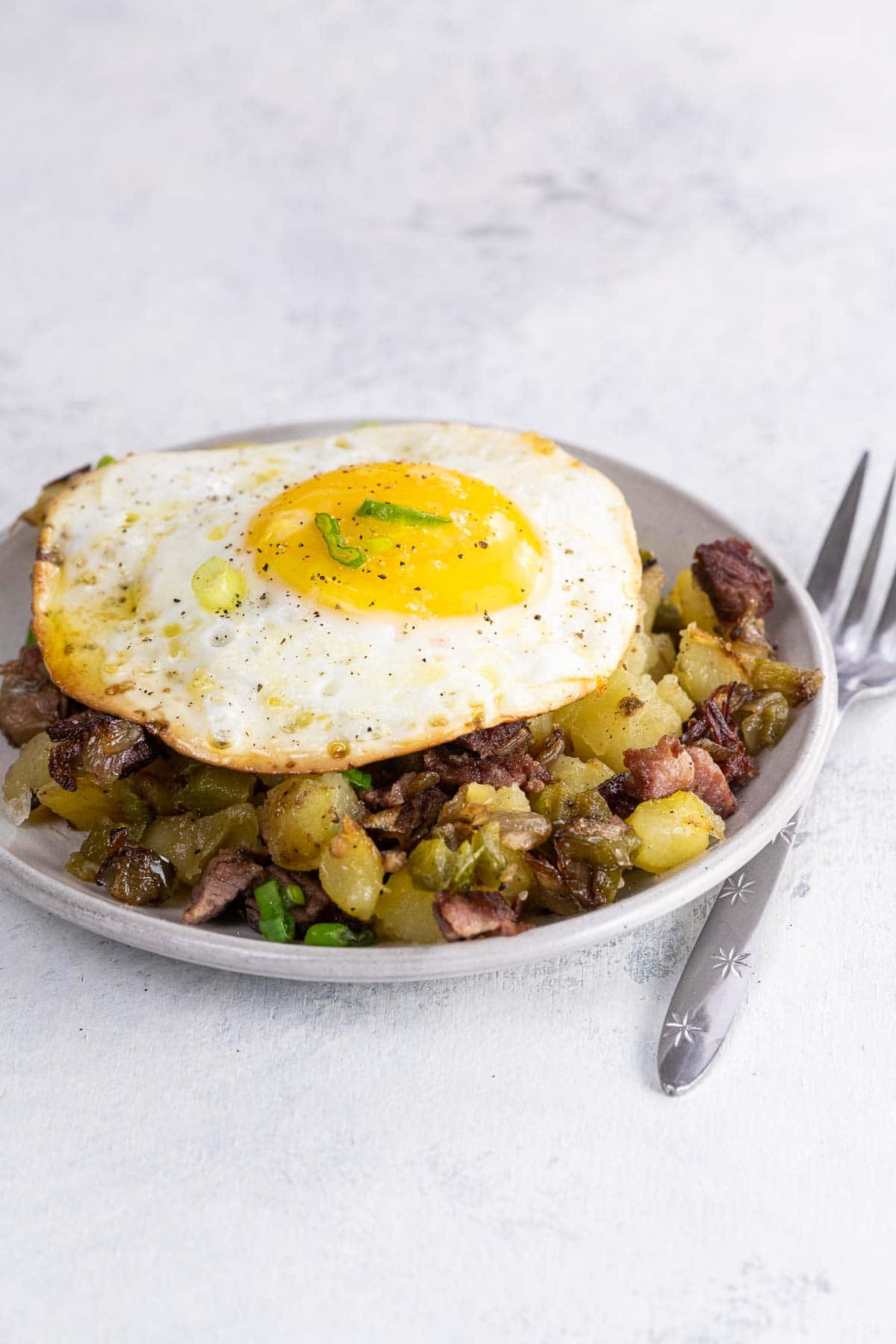 crispy corned beef hash with a sunny side up fried egg on a small plate with a fork