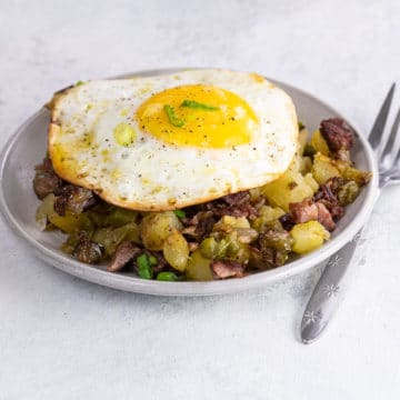 crispy corned beef hash with a sunny side up fried egg on a small plate with a fork