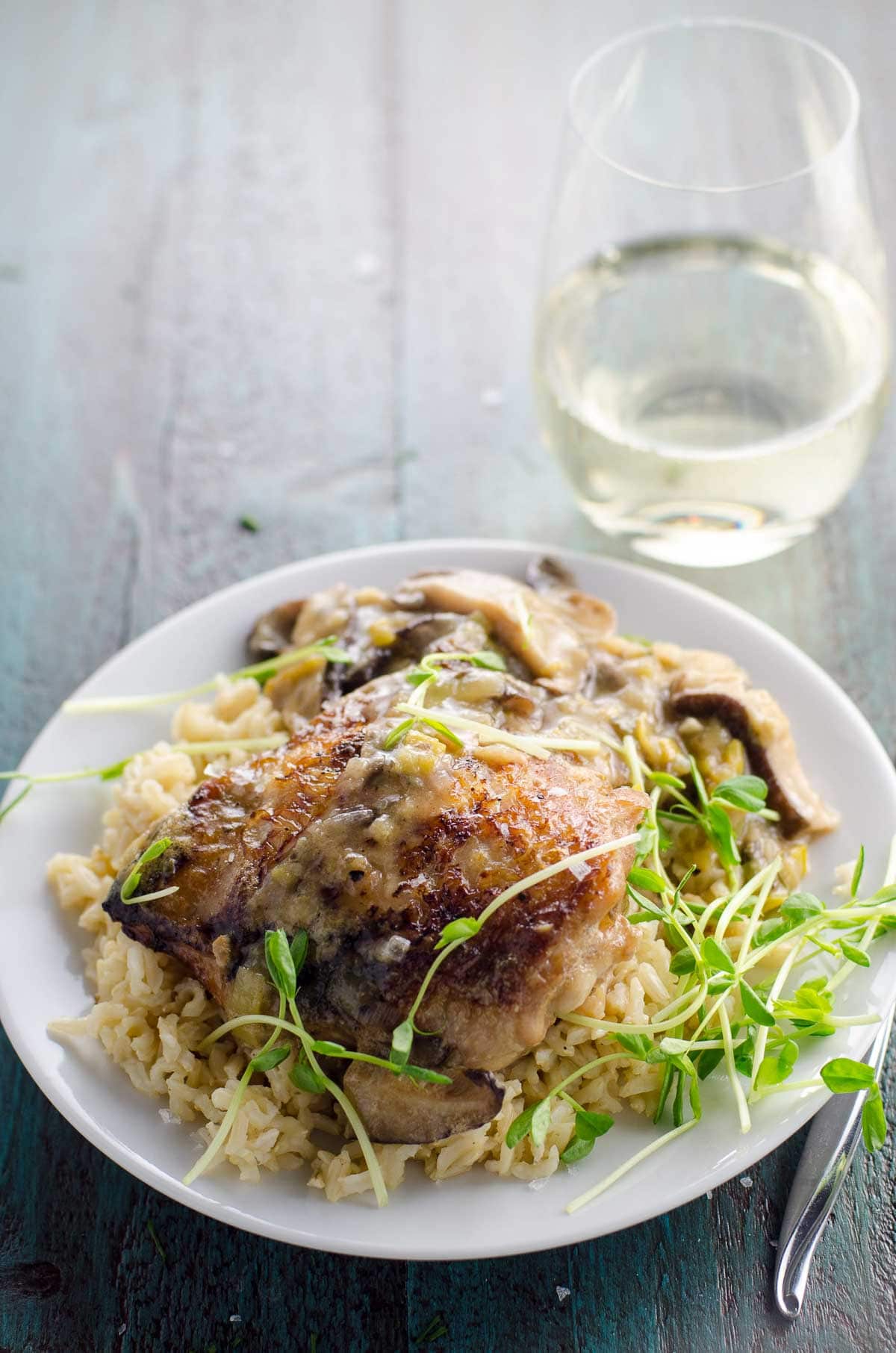 dutch oven chicken thighs with leeks, mushrooms and white wine on a plate with a glass of wine