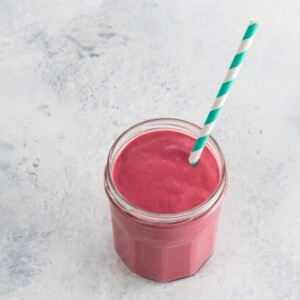 a pink raspberry meyer lemon greek yogurt smoothie in a jam jar glass with a blue and white paper straw