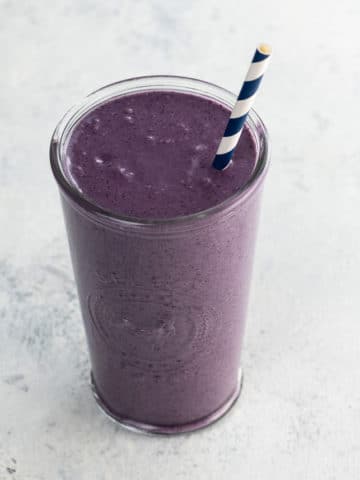 liquid love purple maca smoothie with a blue and white straw in a glass