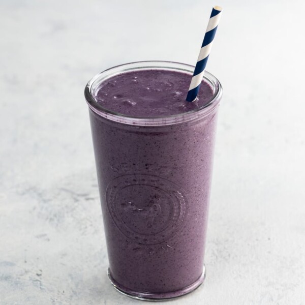 liquid love purple maca smoothie with a blue and white straw in a glass
