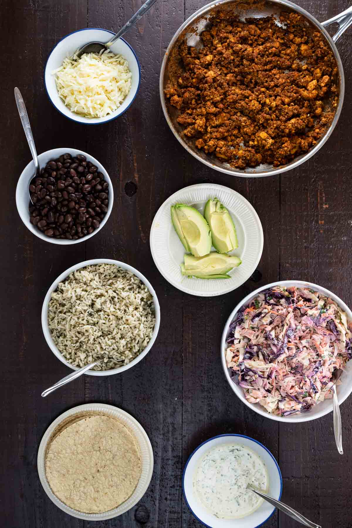 many ingredients for a taco bar laid out in bowls and on plates on a wooden surface