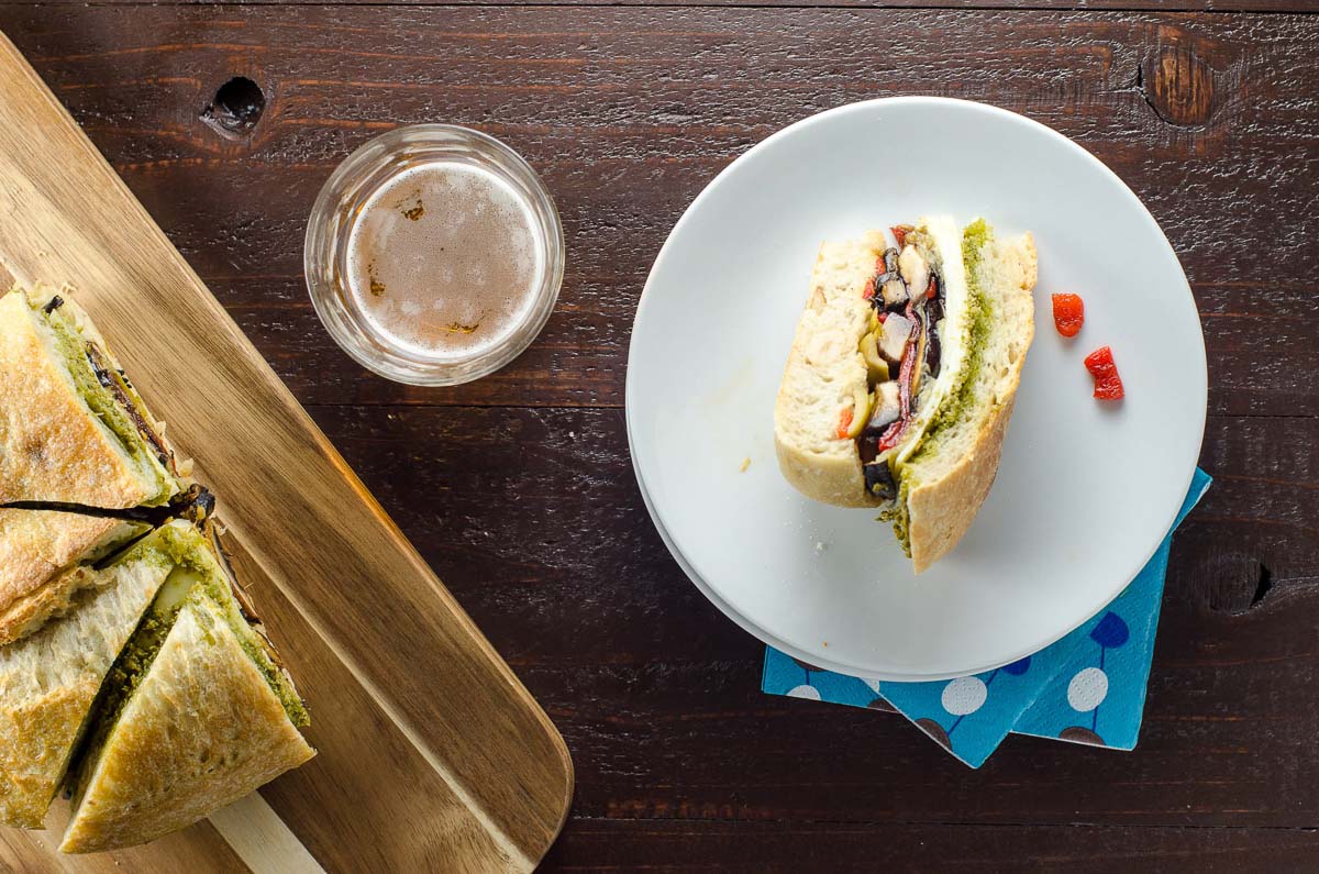 a slice of vegetarian muffaletta on a plate and a glass of beer