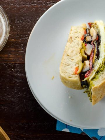 a slice of vegetarian muffaletta on a plate and a glass of beer