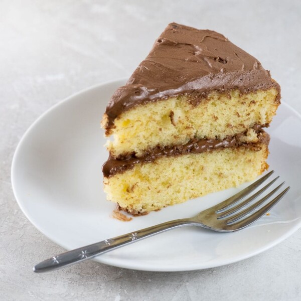 a slice of white wine cake on a plate, with the rest of the cake on a stand in the background
