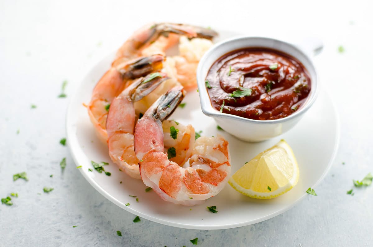 best shrimp cocktail recipe with cocktail sauce and a lemon wedge on a plate
