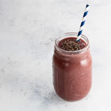 a cherry smoothie with chocolate in a mason jar with a blue and white paper straw