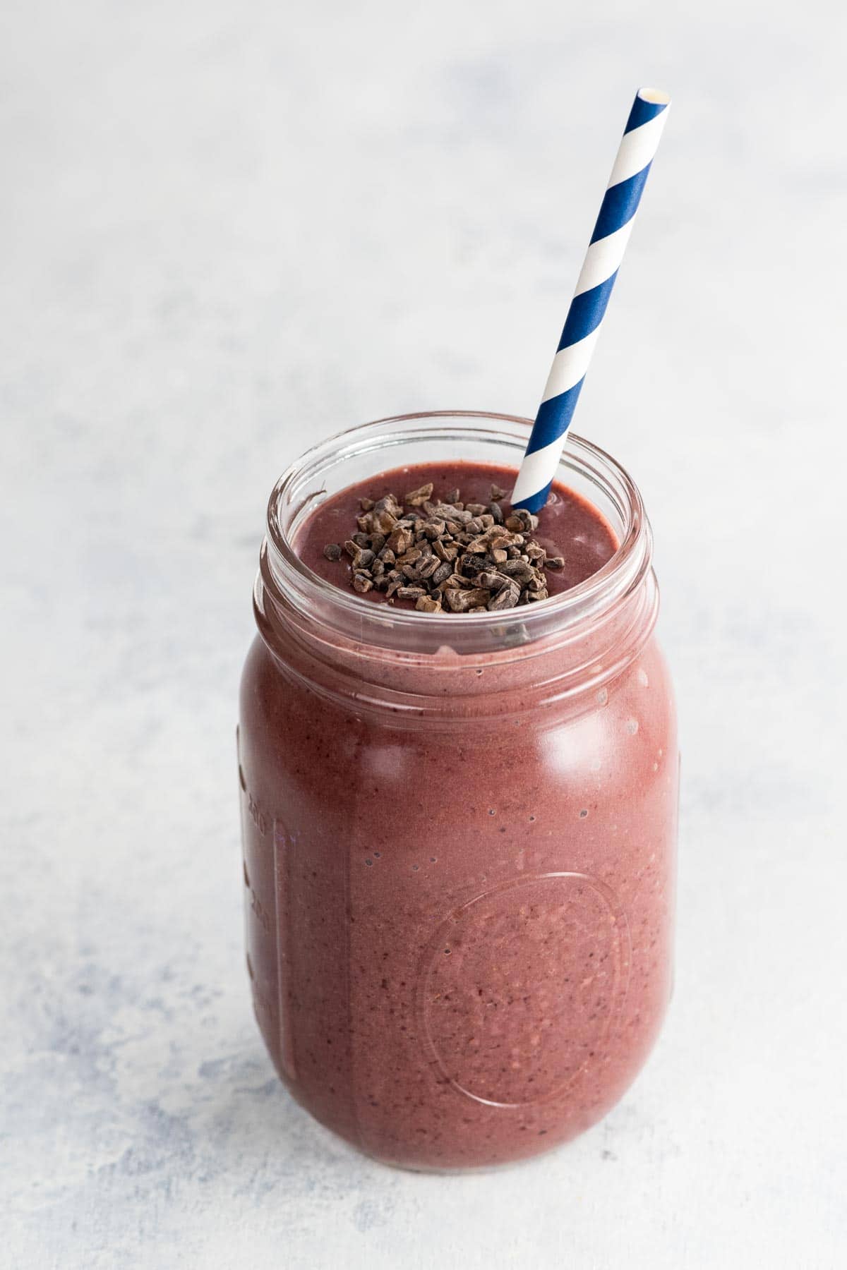 a cherry smoothie with chocolate in a mason jar with a blue and white paper straw