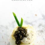a fancy deviled egg with caviar, creme fraiche, and chives on a marble background