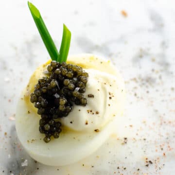 a fancy deviled egg with caviar, creme fraiche, and chives on a marble background