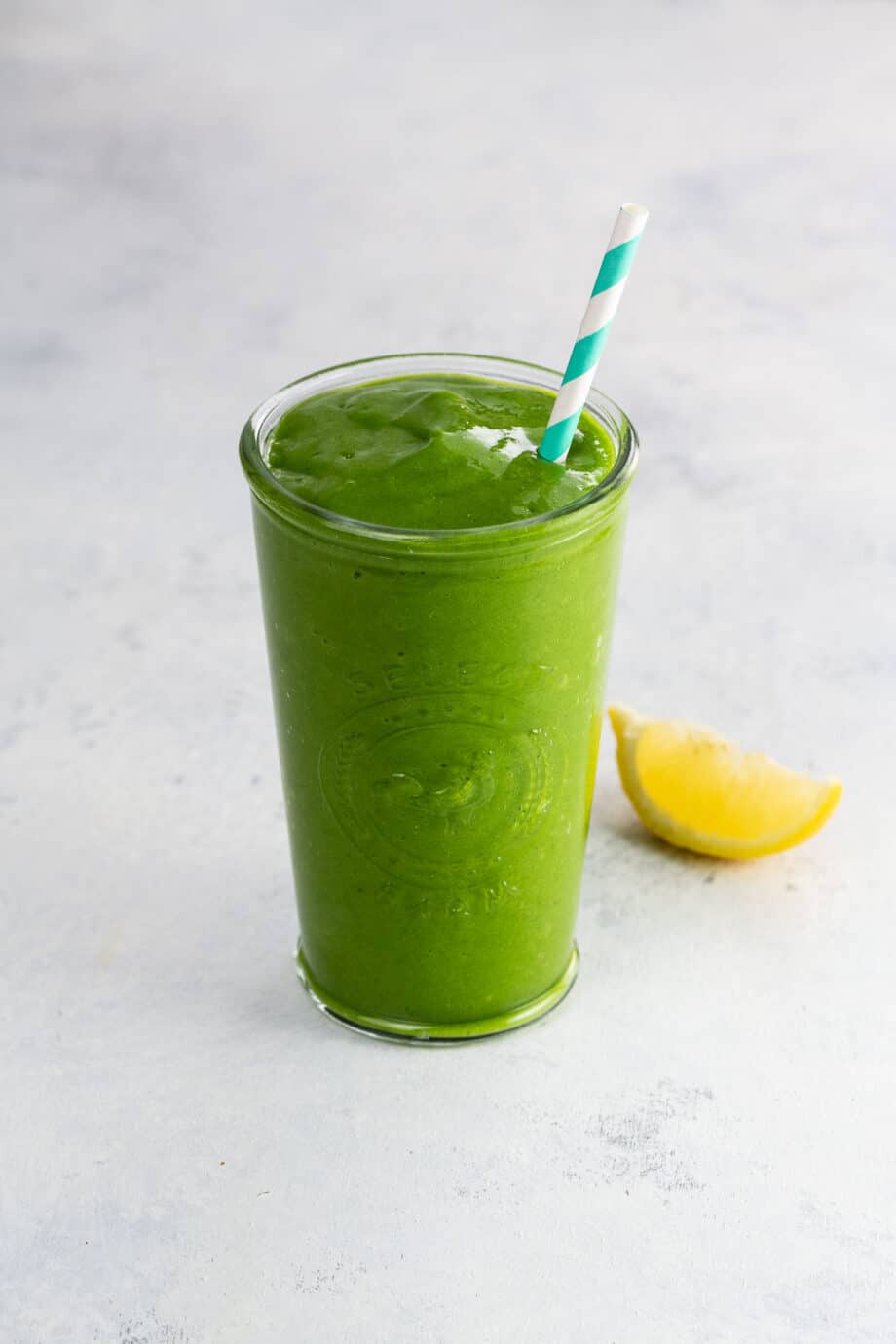 a mango and arugula smoothie in a glass with a paper straw and a lemon wedge