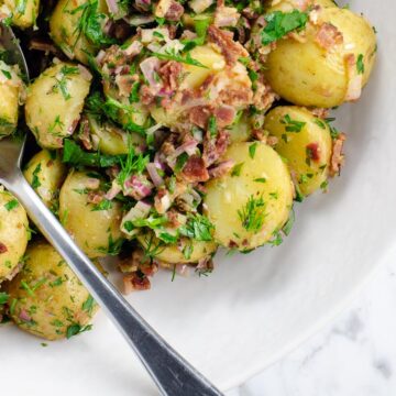 potato salad with bacon and herbs (no mayo) in a bowl with a serving spoon