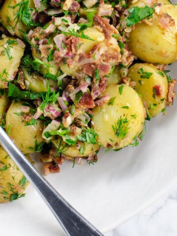potato salad with bacon and herbs (no mayo) in a bowl with a serving spoon