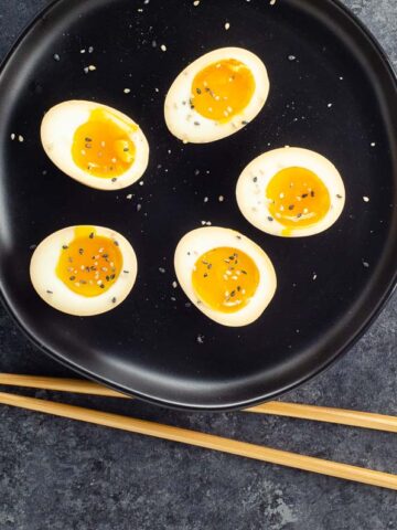 ramen eggs on a black plate with chopsticks