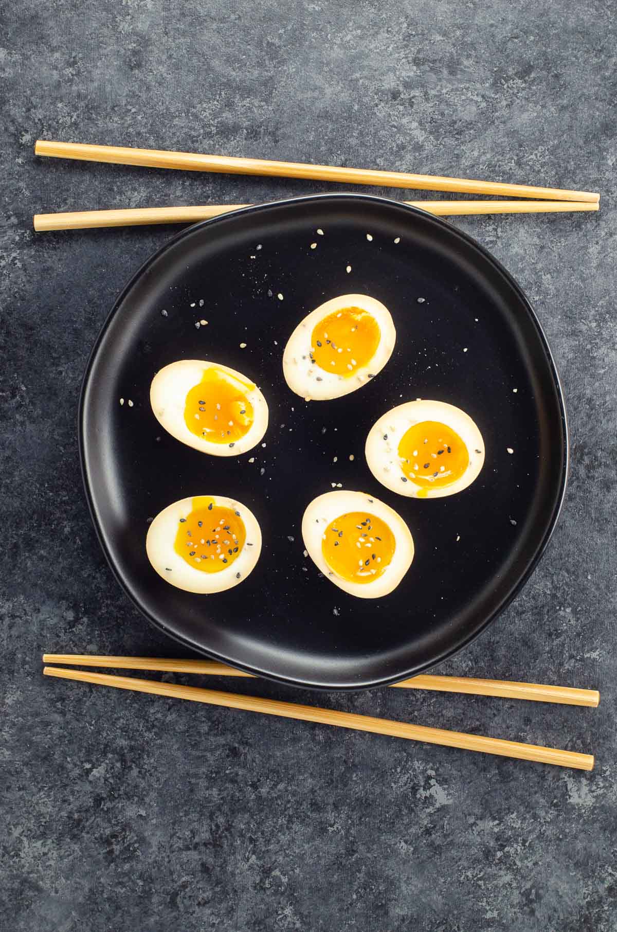 ramen eggs on a black plate with chopsticks