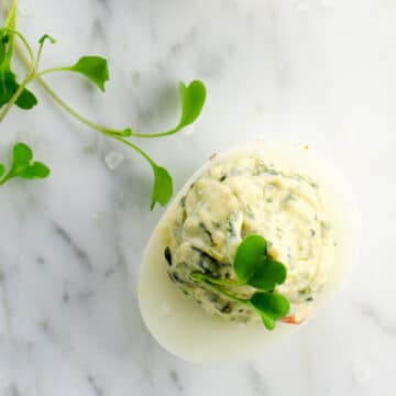 a spinach dip deviled egg and some microgreens on a marble background