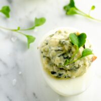 a spinach dip deviled egg and some microgreens on a marble background