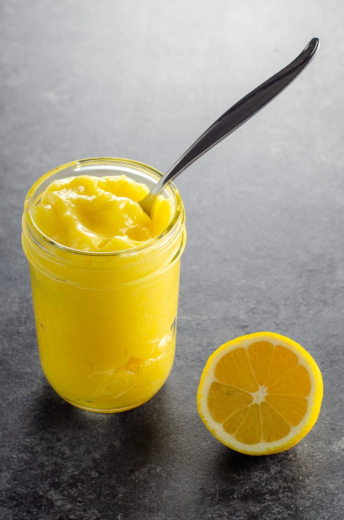 tart lemon curd in a small jar with a spoon and half a lemon