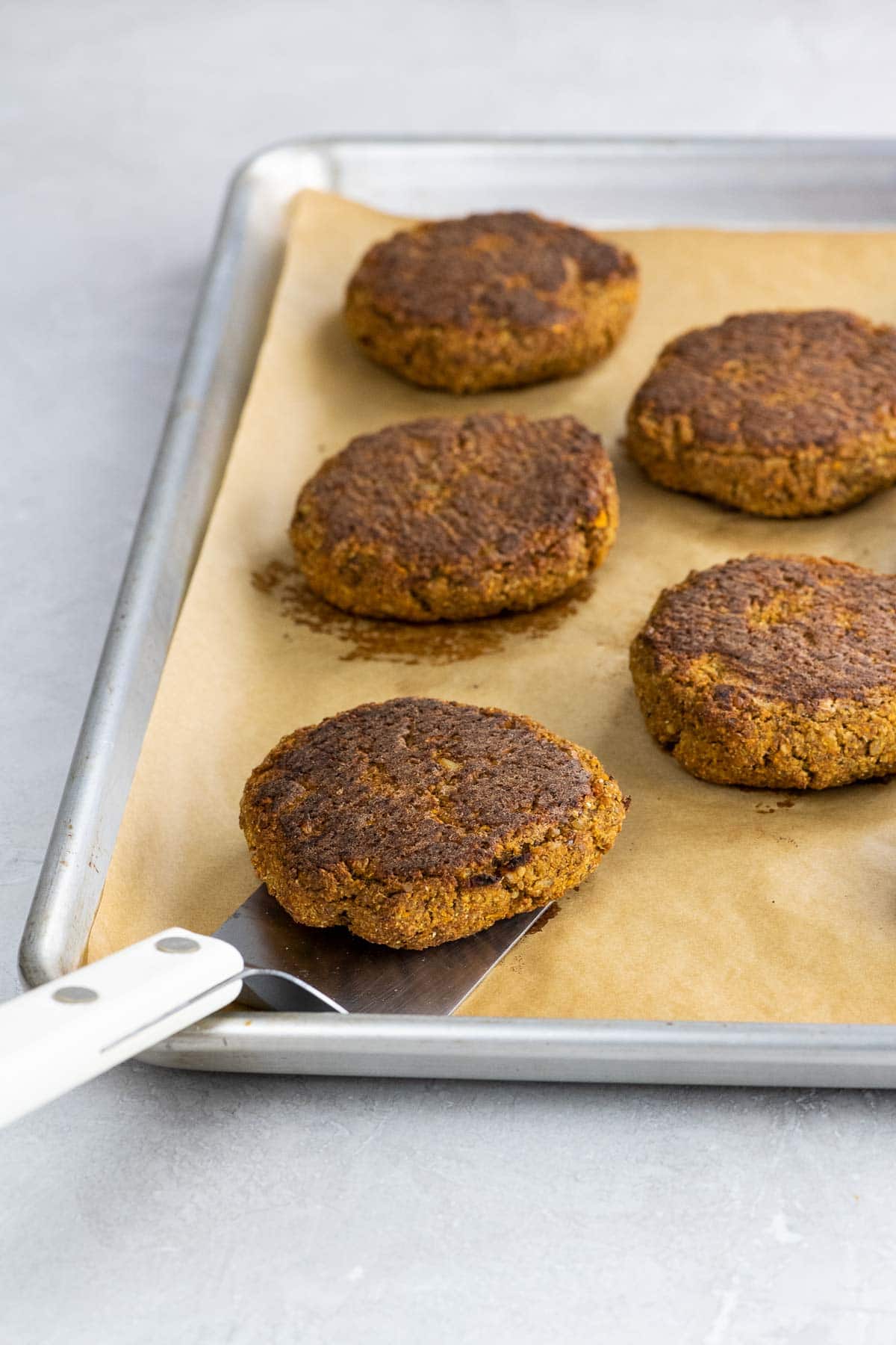 vegan sweet potato lentil burgers on a sheet pan with a spatula
