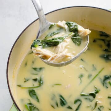 avgolemono soup (greek lemon chicken soup) with orzo and spinach in a pot with a ladle