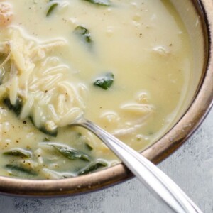 a bowl of avgolemono soup with orzo and spinach, and a spoon