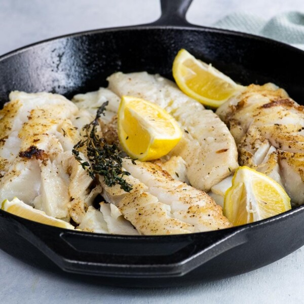 pan fried cod with thyme and lemon wedges in a cast iron skillet