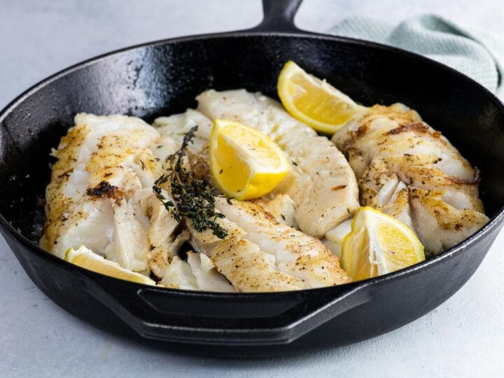 pan fried cod with thyme and lemon wedges in a cast iron skillet