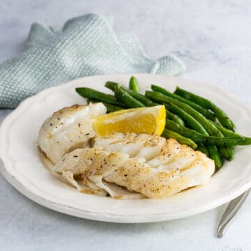 pan fried cod with green beans and a and lemon wedge on a plate