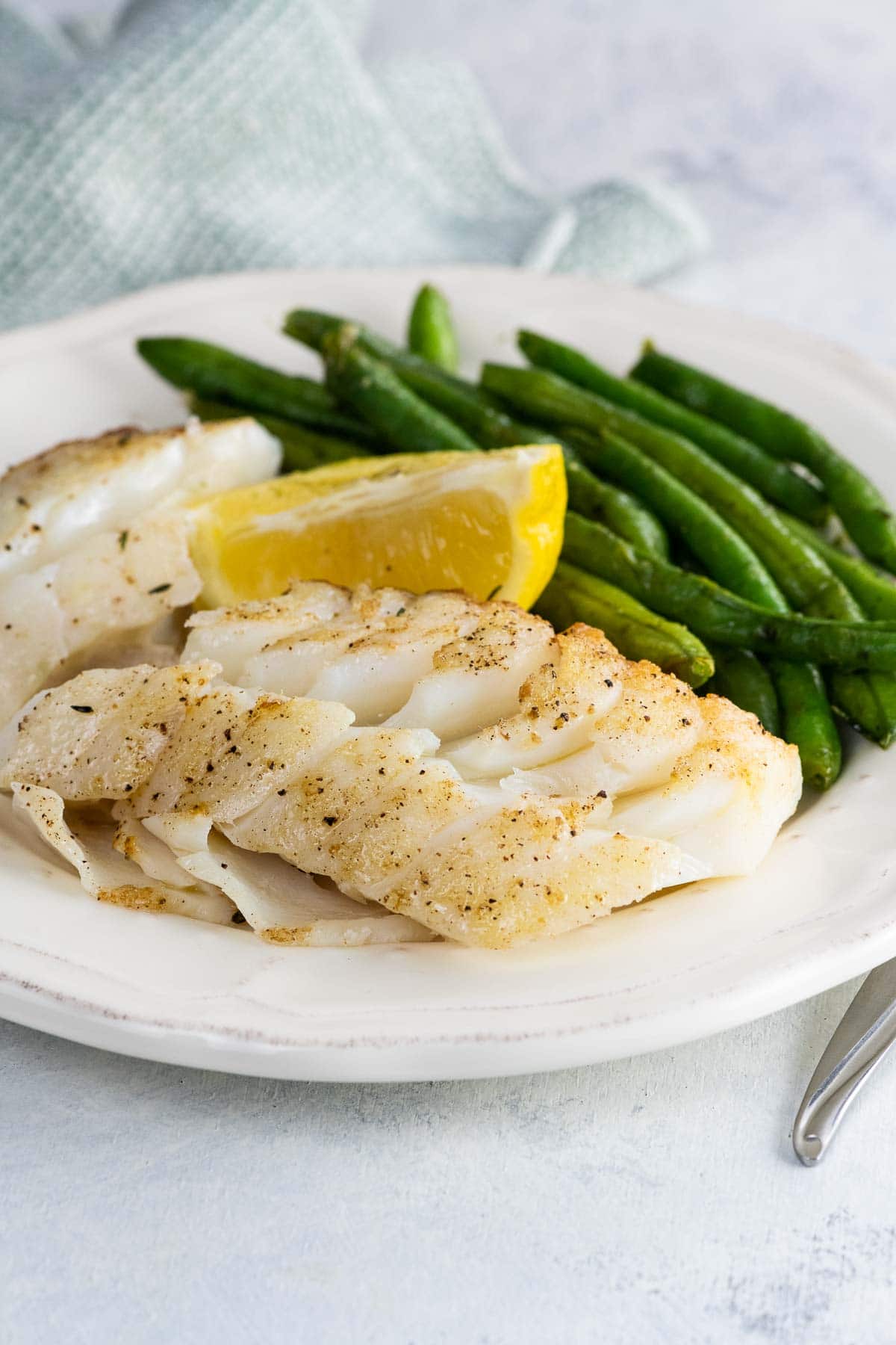 pan fried cod with green beans and a and lemon wedge on a plate