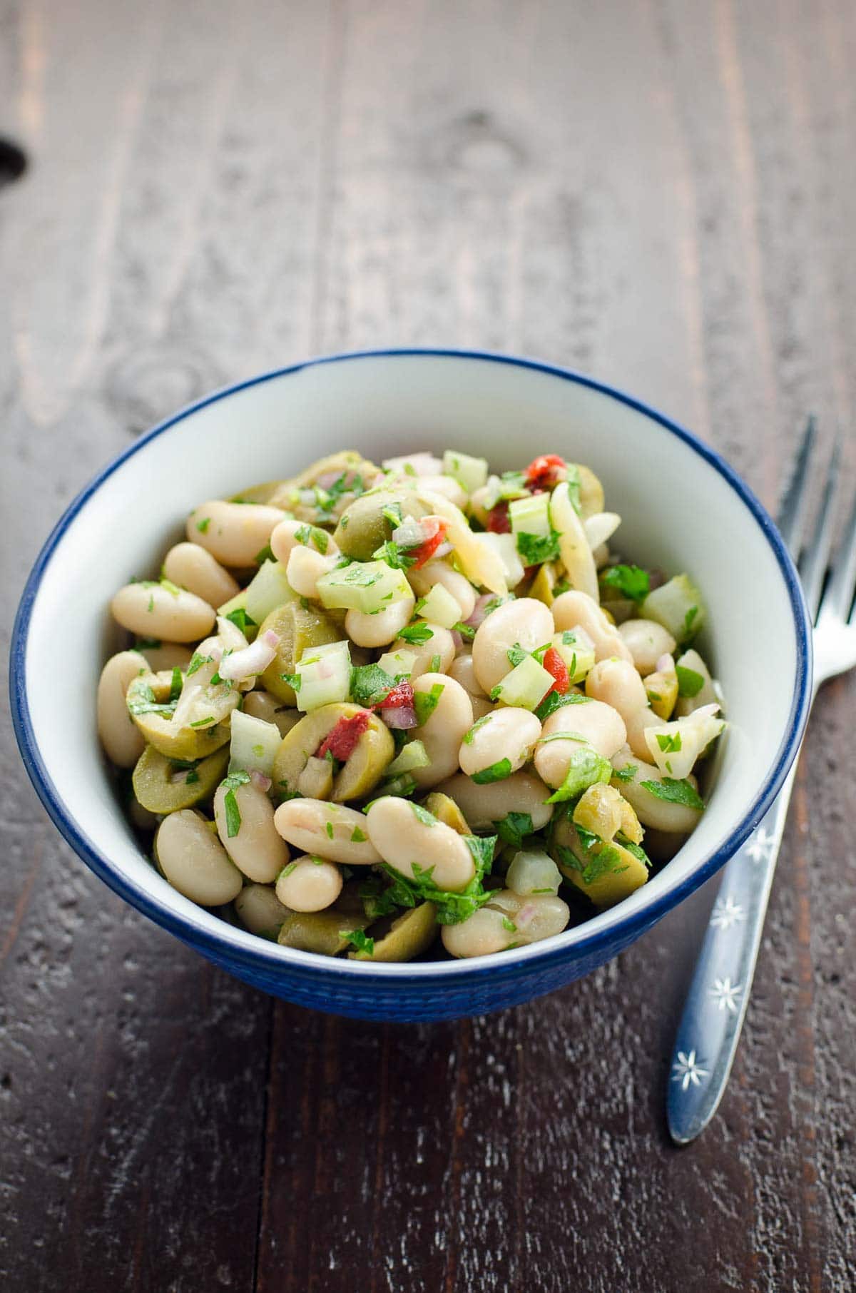 white bean salad with olives in a bowl with a fork